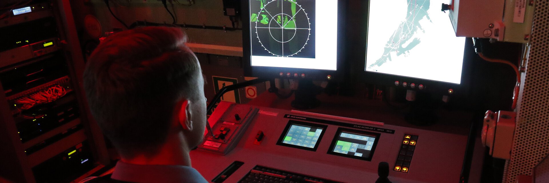 Ein Soldat sitzt vor einem Radarschirm, der Raum ist rot beleuchtet.