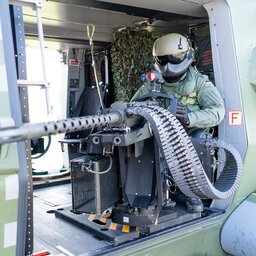 Bordschütze in Uniform sitzt mit Maschinengewehr in der Seitentür eines Hubschraubers