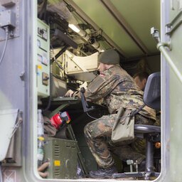 Ein Soldat in Uniform sitzt in einem Metallcontainer, der elektronisches Equipment enthält und schaut auf einen Monitor