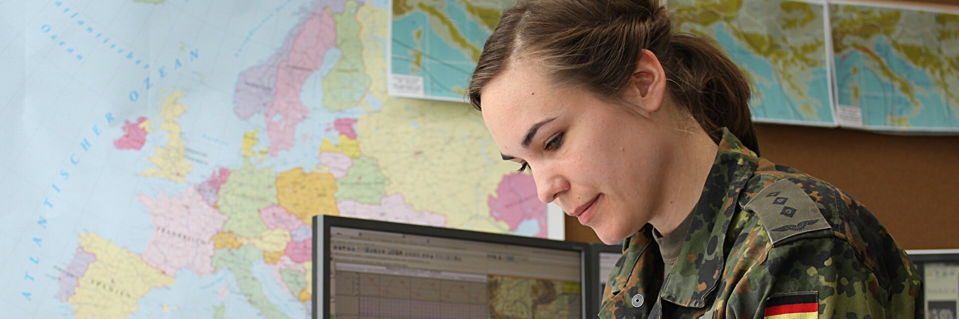 Eine Soldatin sitzt am Schreibtisch und zeichnet etwas auf einer Karte ein