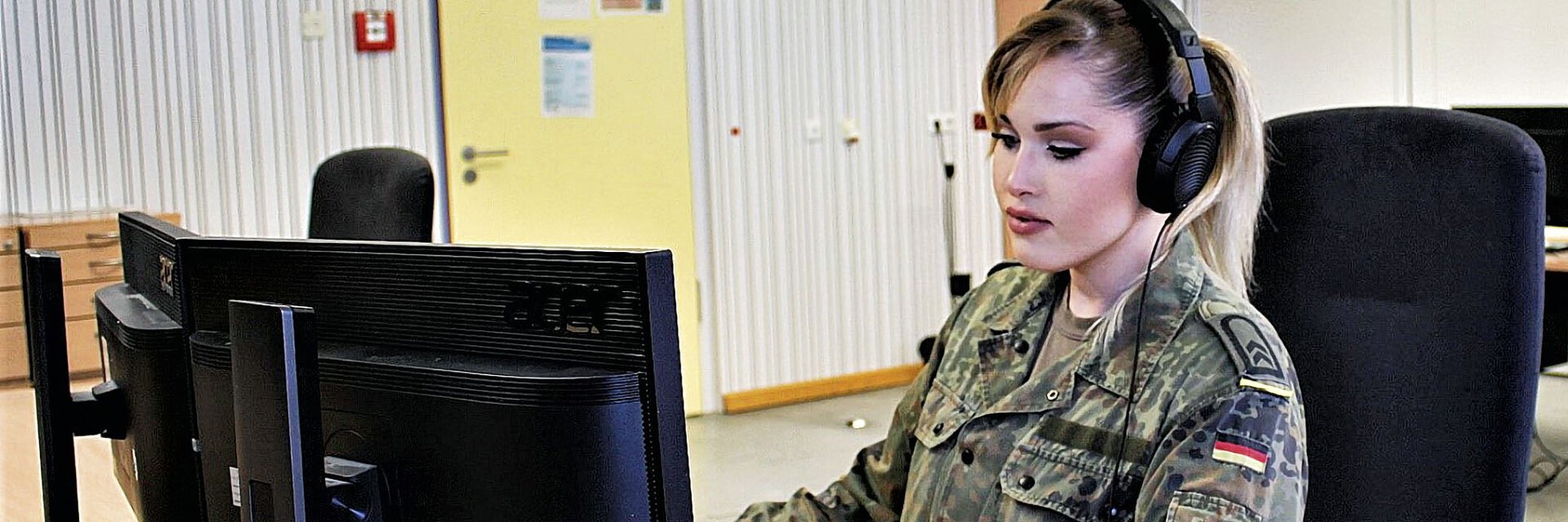 Eine Soldatin sitzt mit Headset vor einem Computer